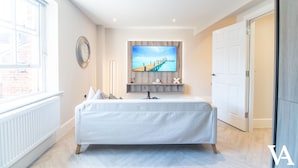 Une chambre moderne avec un grand lit, un téléviseur fixé au mur et une fenêtre donnant sur l’extérieur.