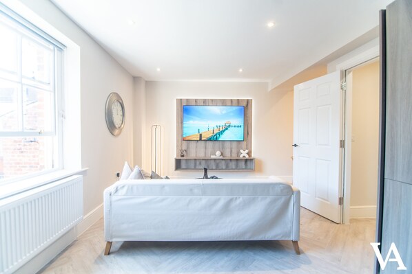 A modern bedroom with a large bed, a television mounted on the wall, and a window providing a view of the outside. - Velvet Apartments - 10 Park Square East (Leeds)