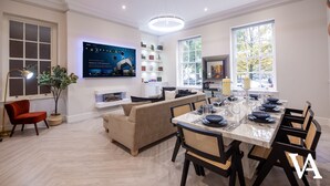 Un salon moderne avec un canapé, une table à manger dressée pour six personnes et un téléviseur fixé au mur.