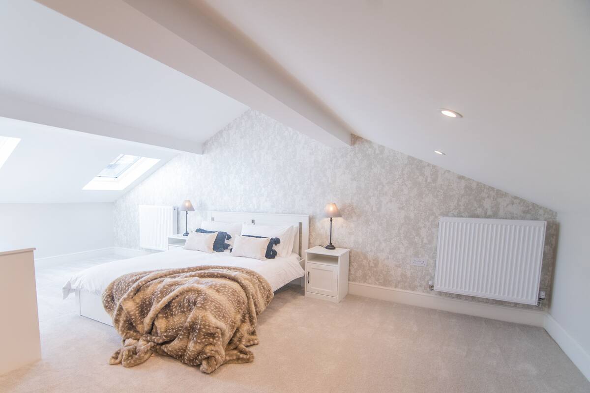 Une chambre moderne avec un plafond en pente, un puits de lumière, un grand lit, des tables de chevet et un radiateur.