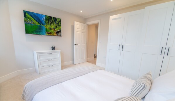A bedroom with a bed, a dresser, a wardrobe, and a painting of a landscape. - Velvet Apartments - 10 Park Square East (Leeds)