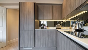 Une cuisine moderne avec des meubles en bois, un four encastré et une bouilloire en acier inoxydable.