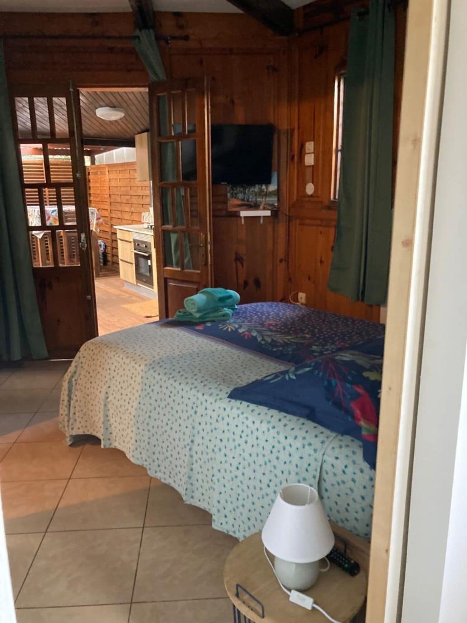 Una habitación tipo cabaña de madera con una cama, un televisor y una mesita con una lámpara.