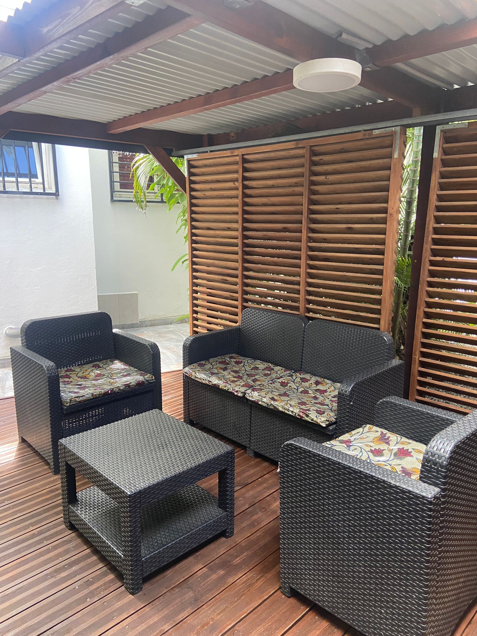 A covered outdoor seating area with wicker furniture and a ceiling fan.