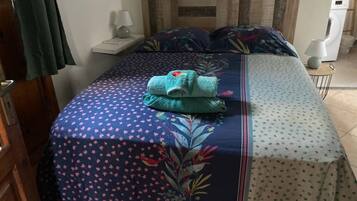 Een net opgemaakt bed met bloemenbedrukking, een opgevouwen handdoek en een nachtkastje met een lamp.