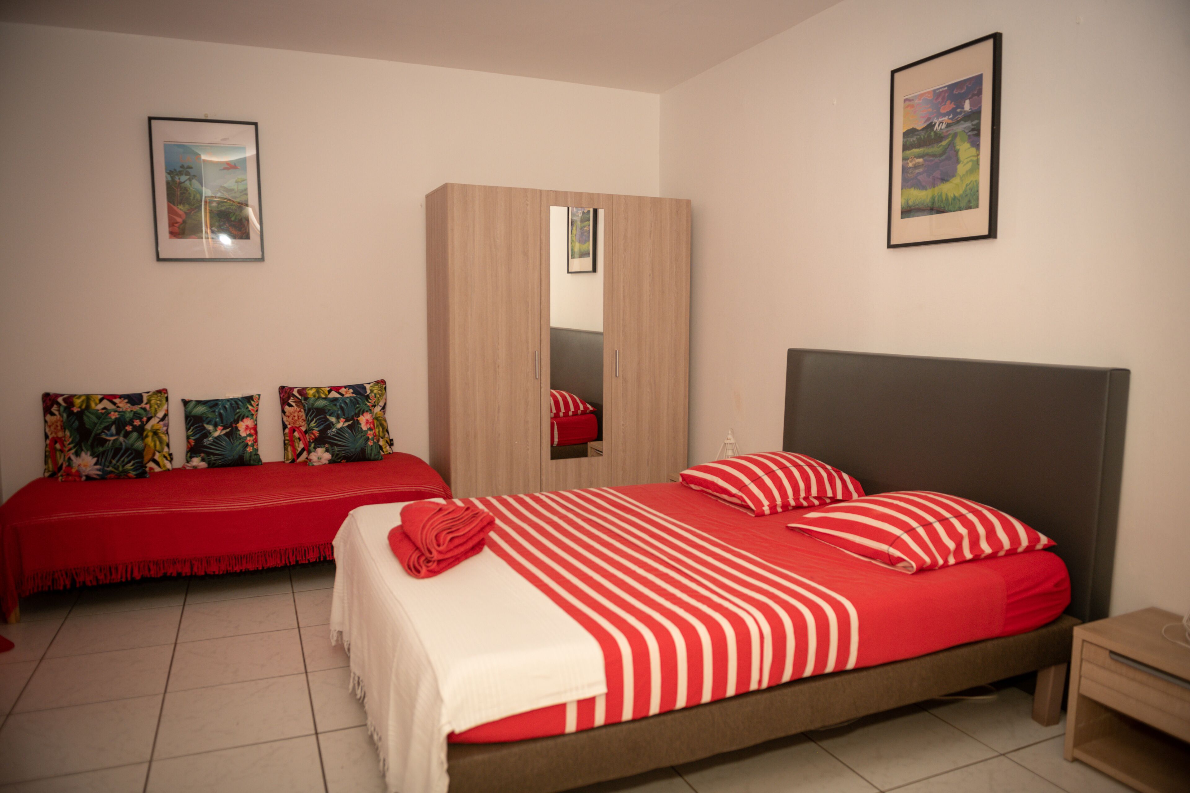 A bedroom with a bed, a bench, a wardrobe, and two framed pictures on the walls.
