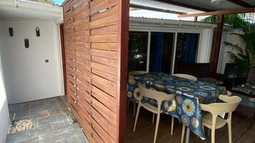 Un'area esterna coperta con un tavolo e sedie di legno, pavimento in piastrelle e tetto in lamiera ondulata.