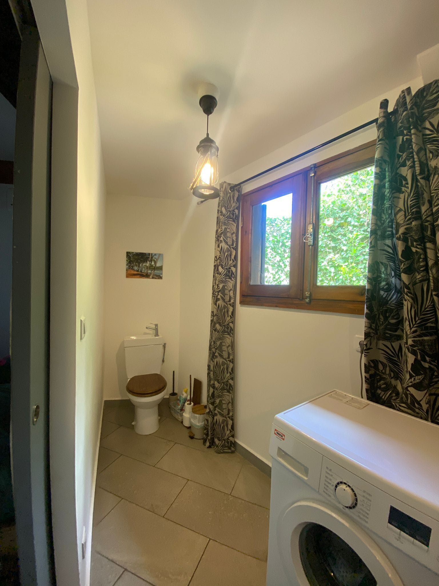 Une petite salle de bain comprenant des toilettes, un lave-linge et un rideau de douche orné d’un motif de feuilles.