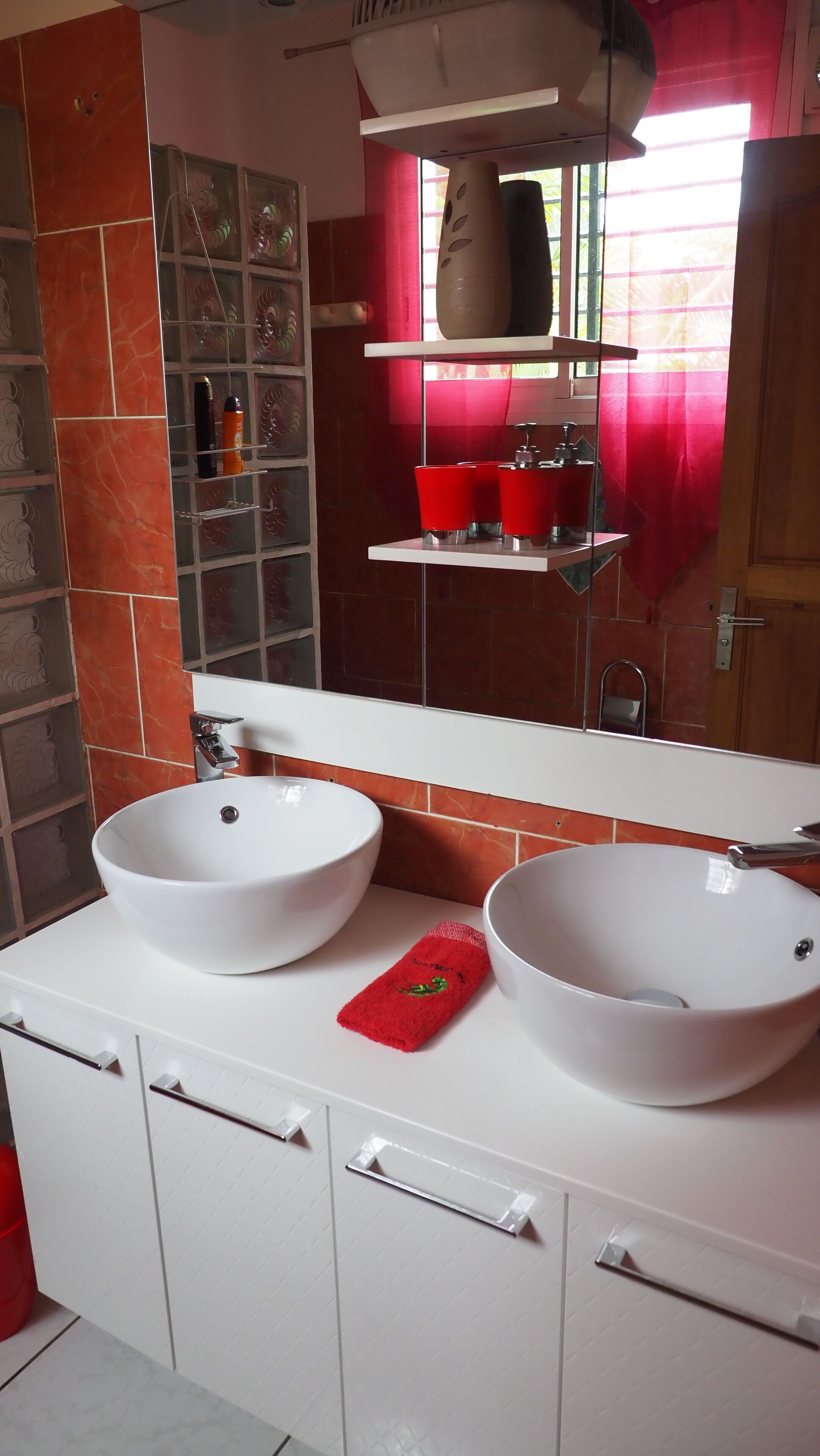 Un bagno con due lavandini bianchi, un asciugamano rosso e uno specchio sopra i lavandini.