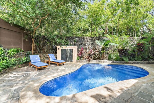 A swimming pool with two lounge chairs, surrounded by lush greenery and a stone wall. - Langosta Beach Club - Casa Pariso by Jet Luxury (Tamarindo)