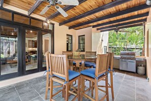 A dining area with a round table and wooden chairs, a ceiling fan, and a view of the outdoors. - Langosta Beach Club - Casa Pariso by Jet Luxury (Tamarindo)