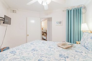 A bedroom with a bed, a desk, a chair, a ceiling fan, a window with curtains, and a door leading to a closet. - Barefootin'-Victorian-Gulf Front-Sleeps 6 (Galveston)