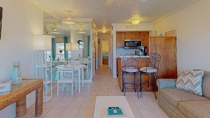 A spacious living area with a dining table and chairs, a kitchen with wooden cabinets, and a ceiling fan. - Barefootin'-Victorian-Gulf Front-Sleeps 6 (Galveston)