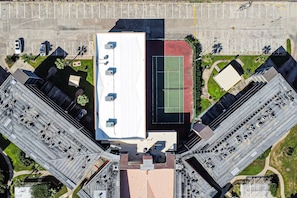 An aerial view of a building with a rooftop terrace, parking lot, and adjacent green spaces.