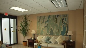 Un hall con un sofá, dos mesitas auxiliares, una mesa de centro de cristal, una planta en maceta y una pared con estampado de camuflaje.