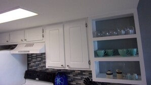 Una cocina con gabinetes blancos, salpicadero de azulejos y una repisa empotrada con cristalería.
