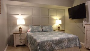 Un dormitorio con cama, dos mesitas de noche con lámparas, un televisor montado en la pared y un aparador.
