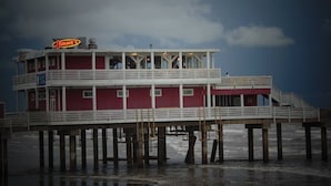 Un muelle con un edificio rojo que tiene un letrero de neón, varias terrazas y vistas al océano.