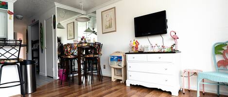A dining area with a wooden table and chairs, a white dresser, and a television mounted on the wall.