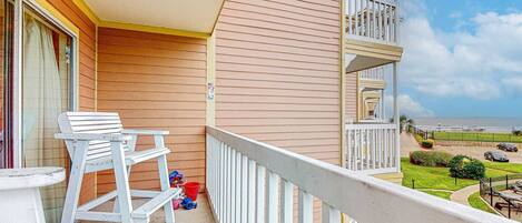 A balcony with white furniture, a view of the beach, and a clear sky.