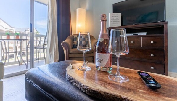 A wooden table with a bottle of wine and two glasses, a remote control, and a television in a hotel room.