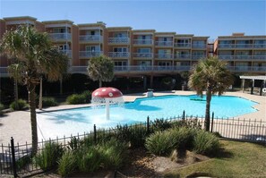 A hotel with a swimming pool, palm trees, and a water fountain.