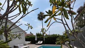 A swimming pool with a wooden deck, lounge chairs, and a white building in the background.