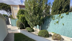 A well-maintained garden with a lawn, a tiled patio, and a green fence.
