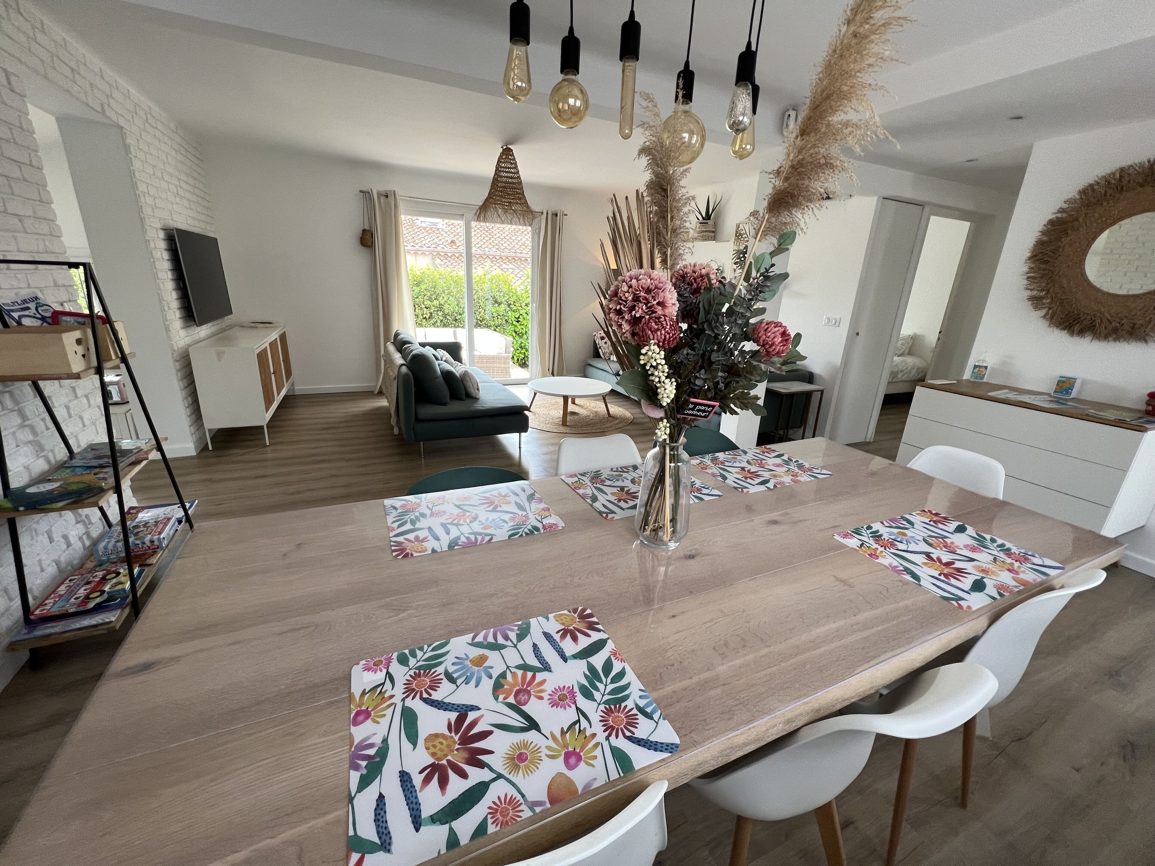 A modern dining area with a wooden table, white chairs, and floral placemats.