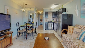 A modern kitchen with stainless steel appliances, a dining area with a wooden table and chairs, and a living room with a sofa and a television. - Makin' Memories @ Victorian (GVR05004) (Galveston)