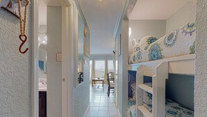A narrow hallway with bunk beds on one side and a door leading to a bathroom. - Makin' Memories @ Victorian (GVR05004) (Galveston)