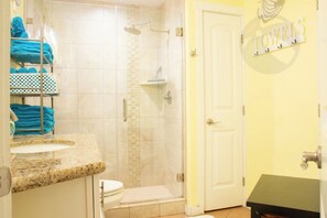 Ein Badezimmer mit Dusche, Waschbecken und Toilette. Blaue Handtücher liegen auf einem Ablagegestell.