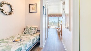 A narrow hallway leading to a balcony with a view, a bed with a tropical print bedspread, and a framed picture on the wall.