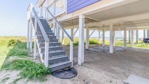 A coastal house with a covered porch, a staircase leading to a deck, and a view of the beach. - Purple Pearl - (GVR06919) (Galveston)
