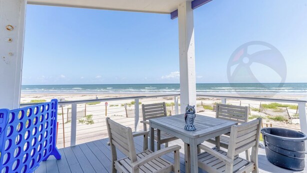 A covered outdoor seating area with a table and chairs, overlooking a beach. - Purple Pearl - (GVR06919) (Galveston)