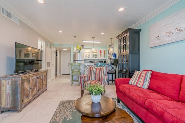 A spacious living room with a red sofa, a television, and a kitchen in the background.
