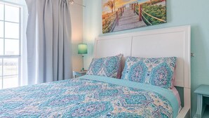 Un dormitorio con cama, mesita de noche, un cuadro y ventana con cortinas.
