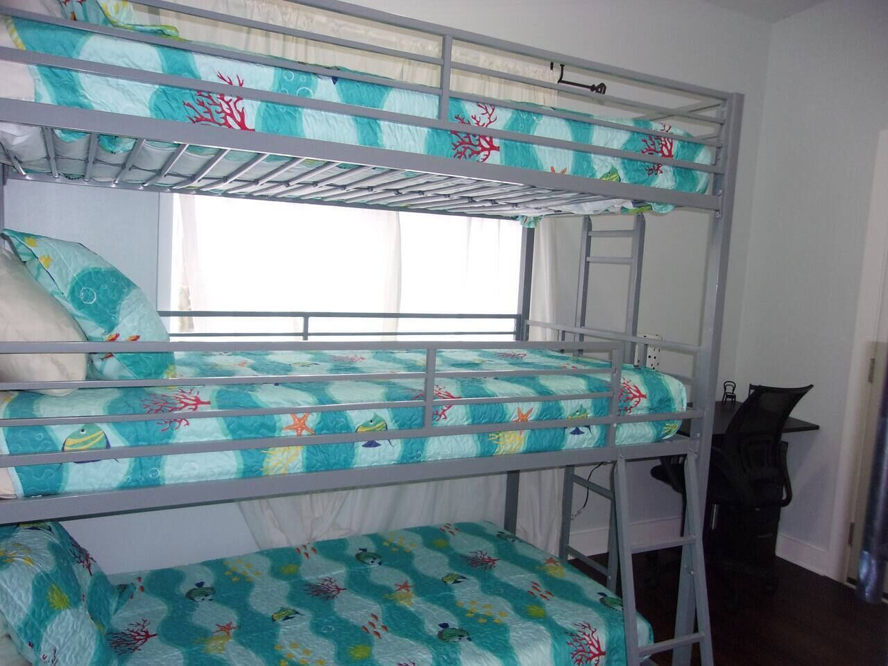 A bunk bed with a window view, a desk, and a chair in a room.
