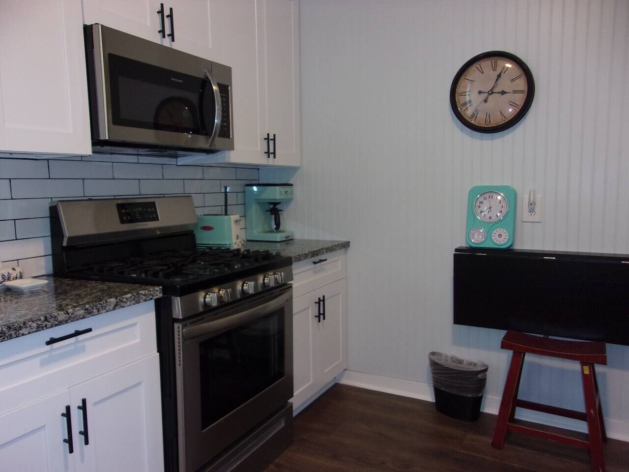 A kitchen with white cabinets, a stainless steel stove, a microwave, a coffee maker, and a clock on the wall.