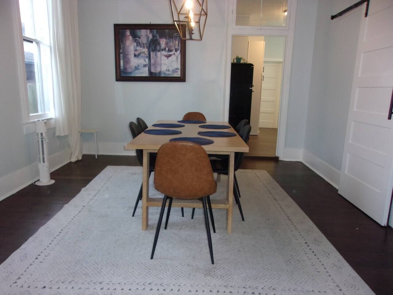 Een eethoek met een tafel en stoelen, een wit vloerkleed, een schilderij aan de muur en een deur op de achtergrond.