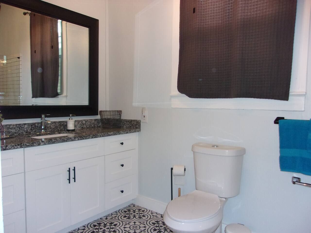 Un baño con inodoro blanco, lavabo con encimera de granito y espejo sobre el lavabo.