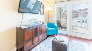 Ein Wohnzimmer mit Holzschrank, blauem Sessel, Flachbildfernseher und einer Glasschiebetür, die auf einen Balkon führt.