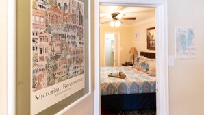 Eine gerahmte Karte der Galveston Island im Stil der viktorianischen Renaissance, ein Schlafzimmer mit einem gemusterten Bettbezug und einem Deckenventilator.