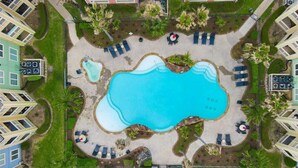 Vue aérienne d’un hôtel doté d’une piscine centrale, entourée d’espaces de détente et de palmiers.