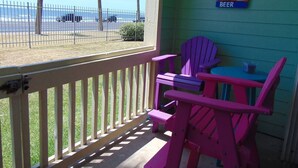 A porch with a view of the beach, a sign encouraging to save water, drink beer, and drink beer, and two pink Adirondack chairs. - Surf's Up at the Dawn BEACH FRONT (Galveston)