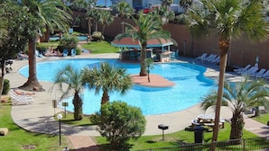 A swimming pool with a curved design, surrounded by palm trees and lounge chairs. - Welcome Inn at Maravilla! (Galveston)