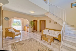 A spacious living area with a checkered floor, a staircase, wicker furniture, and a view through a large window. - Casa Vista Cumeada - Peaceful Hillside Villa (Silves)