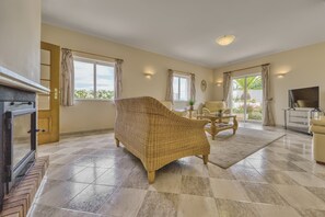 A spacious living room with a large wicker sofa, a wooden coffee table, and a television. - Casa Vista Cumeada - Peaceful Hillside Villa (Silves)