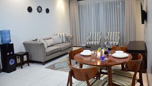 A modern living room with a sofa, dining table, chairs, and a water dispenser. - Yohana Residences (Nairobi)