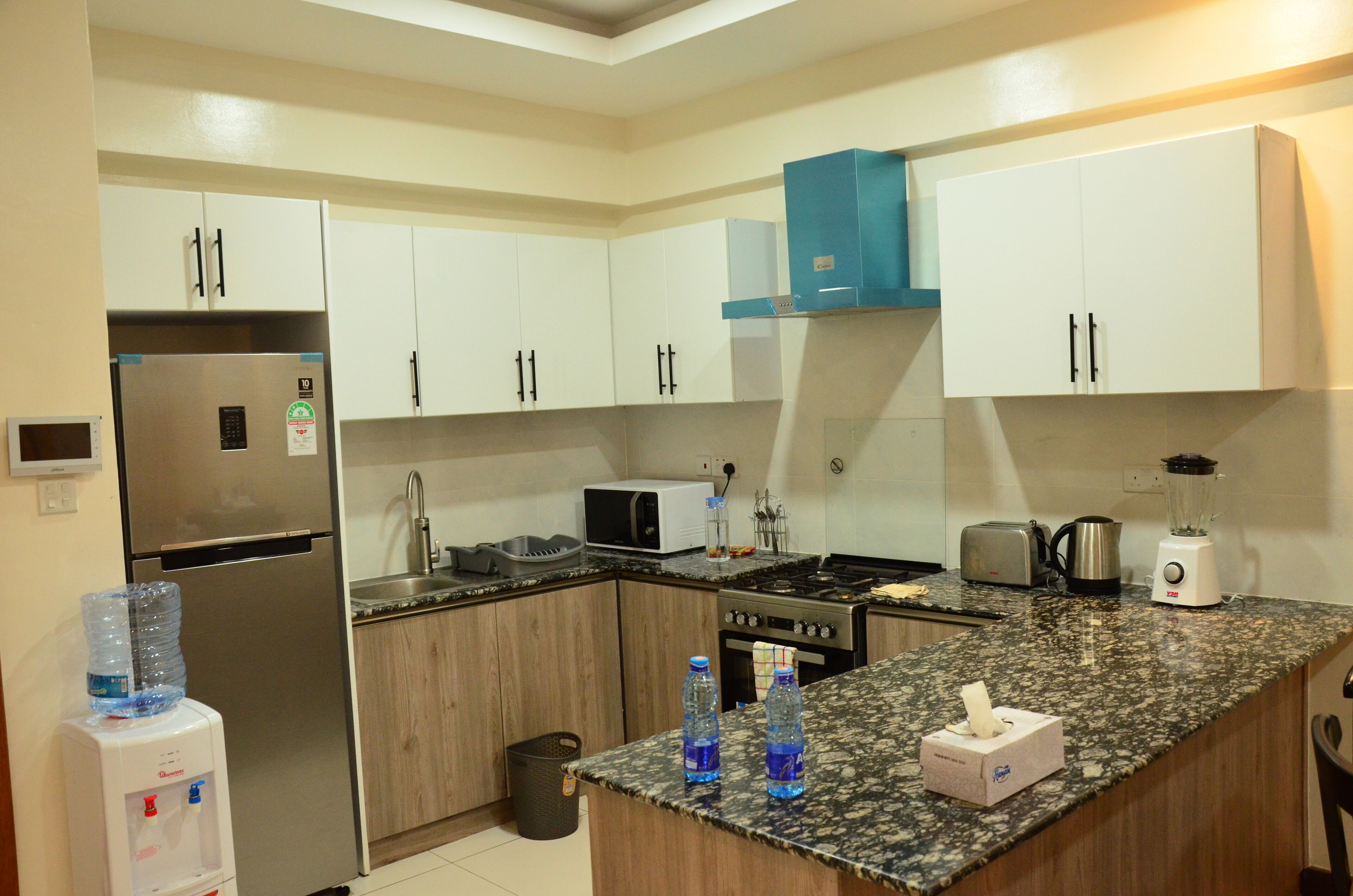 A modern kitchen with white cabinets, a stainless steel refrigerator, a microwave, a stove, and a blender.